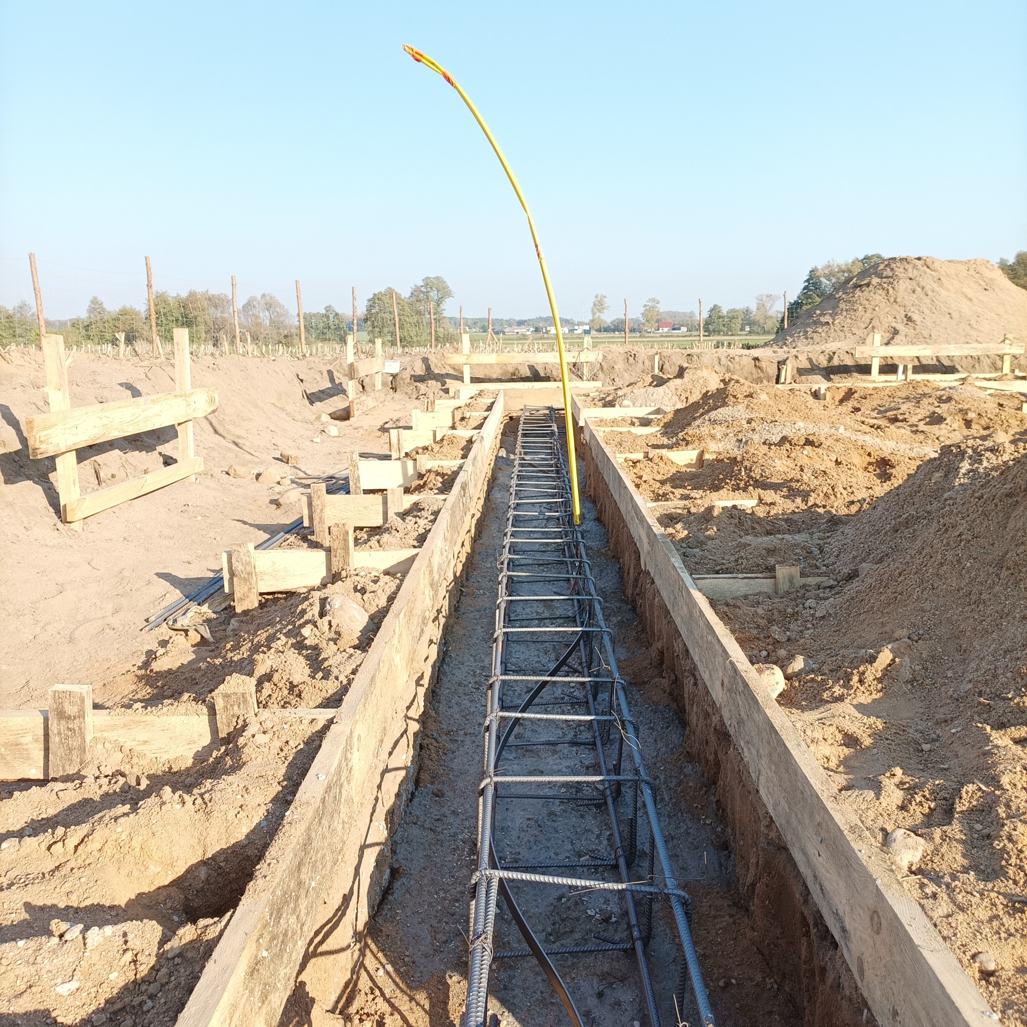 Zbrojenie w wykopie fundamentowym, przygotowane do zalania betonem, z żółtym kablem oznaczającym przebieg instalacji, widok z góry.