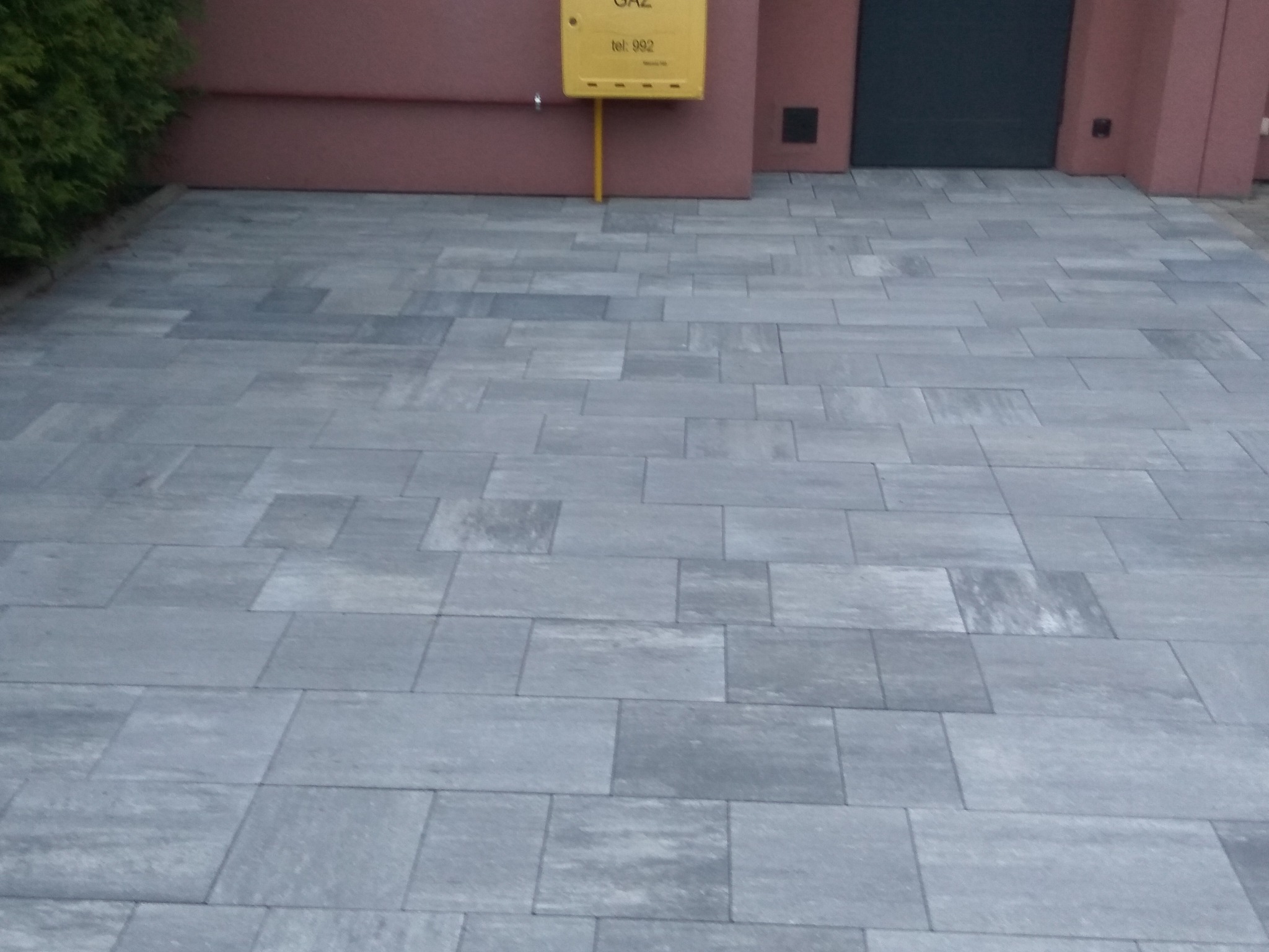 Ułożony wjazd z szarej kostki brukowej, widoczna skrzynka gazowa na elewacji budynku.