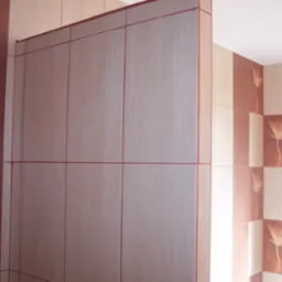 Wykończona ściana w łazience z szarych płytek ceramicznych z bordową fugą i dekoracyjnymi płytkami z motywem kwiatowym na sąsiedniej ścianie.