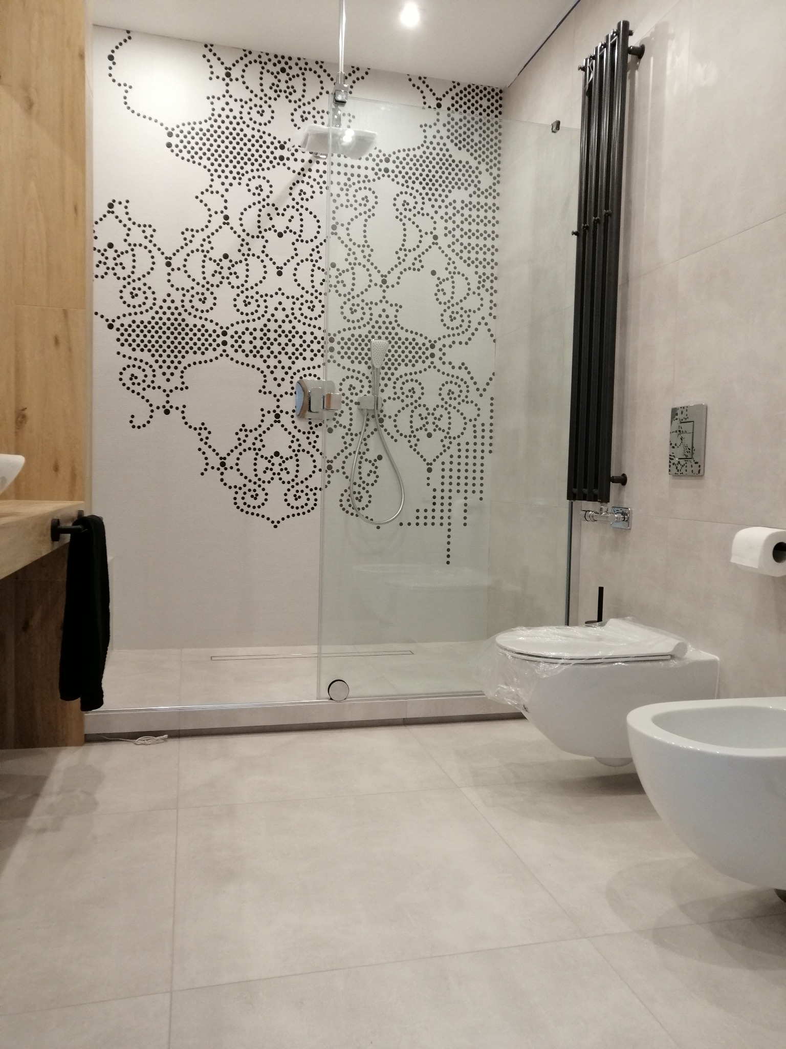 Nowoczesna łazienka z kabiną prysznicową typu walk-in z dekoracyjną ścianą w kropki, wiszącą toaletą i bidetem. Na ścianie grzejnik drabinkowy.