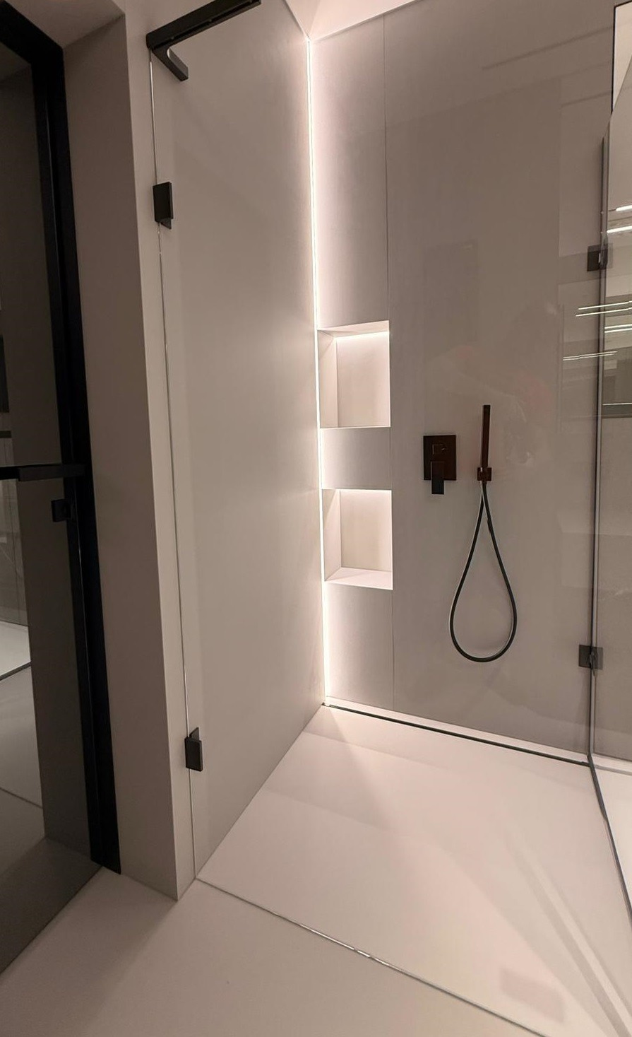 Minimalistyczna kabina prysznicowa z wnękami podświetlanymi LED, czarna armatura i szklane drzwi. Nowoczesny design, jasne płytki, subtelne oświetlenie.