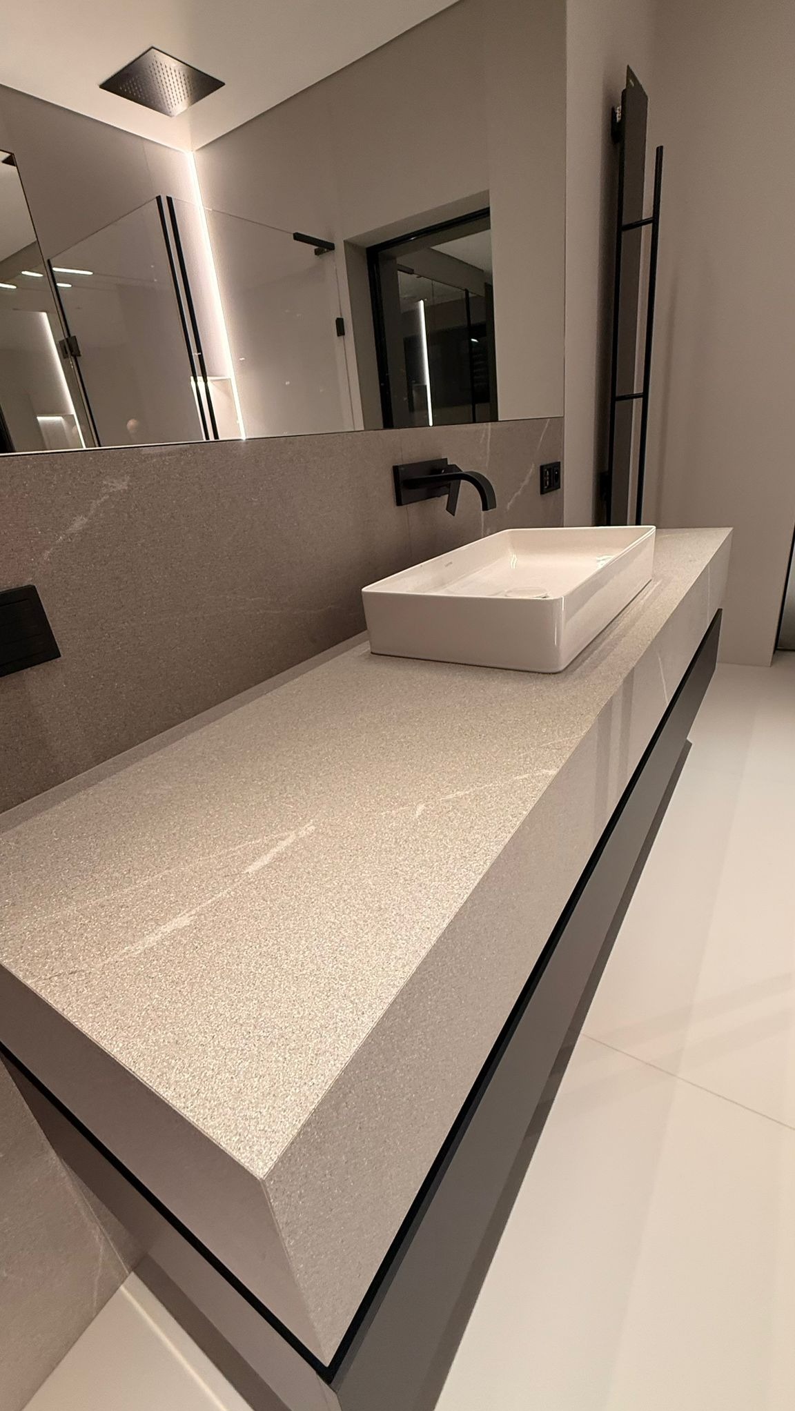 Nowoczesna łazienka z blatem z konglomeratu i prostokątną umywalką nablatową. Czarna armatura i minimalistyczne oświetlenie LED.