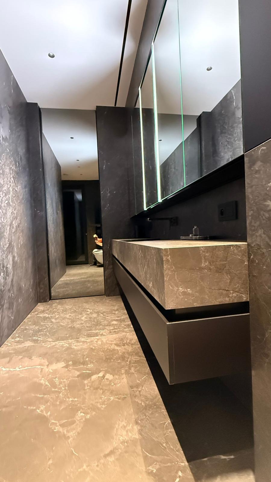 Nowoczesna łazienka w odcieniach szarości z marmurową umywalką i lustrami z podświetleniem LED. Widok z perspektywy podłogi, ukazujący fakturę płytek.