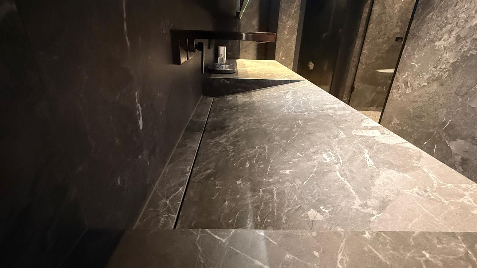 Marmurowa umywalka z ukrytym odpływem liniowym i minimalistyczną baterią w ciemnej łazience. Nowoczesne wykończenie z dbałością o detale.