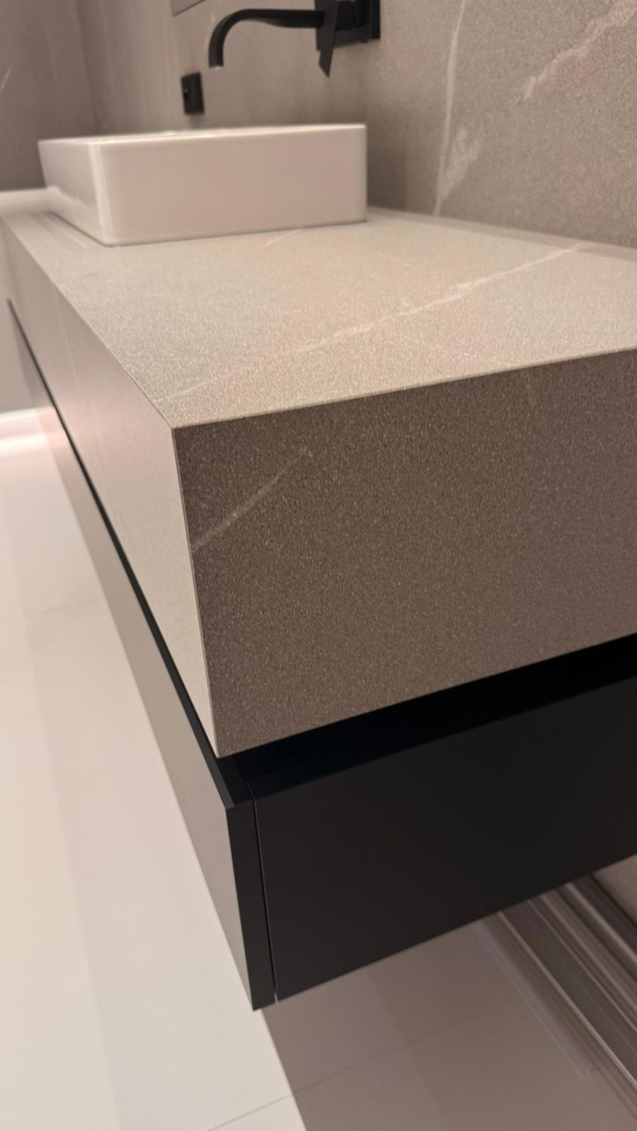 Minimalistyczna łazienka: blat z szarego kamienia, biała umywalka i czarna bateria. Nowoczesne wykończenie, subtelne oświetlenie LED pod szafką.