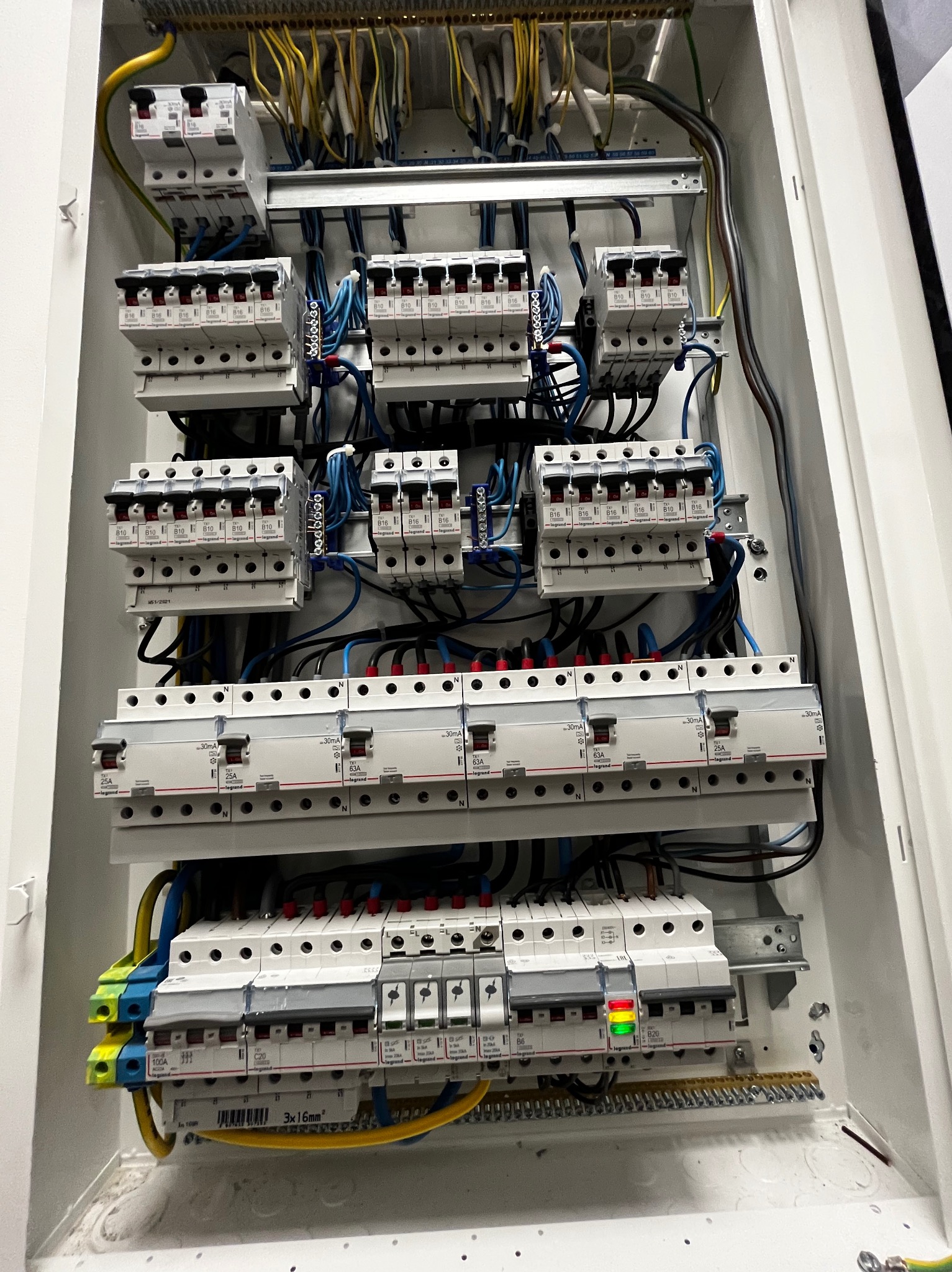 Otwarta, biała skrzynka rozdzielcza z zamontowanymi bezpiecznikami i przewodami elektrycznymi w różnych kolorach, widok z bliska na ułożone rzędy zabezpieczeń z oznaczeniami i podłączeniami.