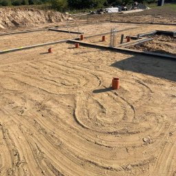Hydro-Pro Paweł Garwoła - Przygotowanie podłoża pod budowę domu: widoczne fundamenty, wystające rury kanalizacyjne i ślady po ułożeniu instalacji w piasku.