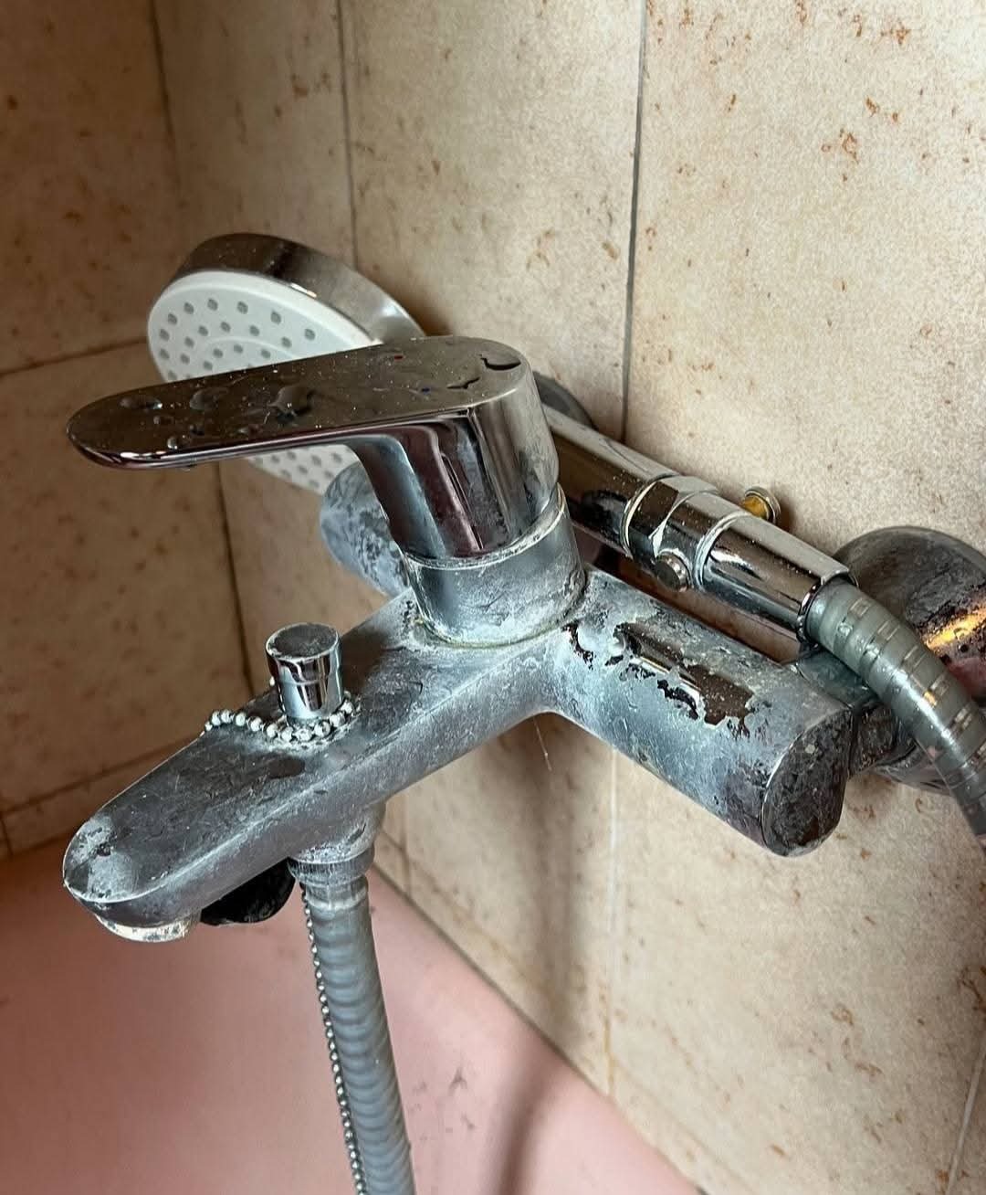 Zakamieniona bateria wannowa z prysznicem, widoczne ślady po odkamienianiu, płytki ceramiczne w tle.