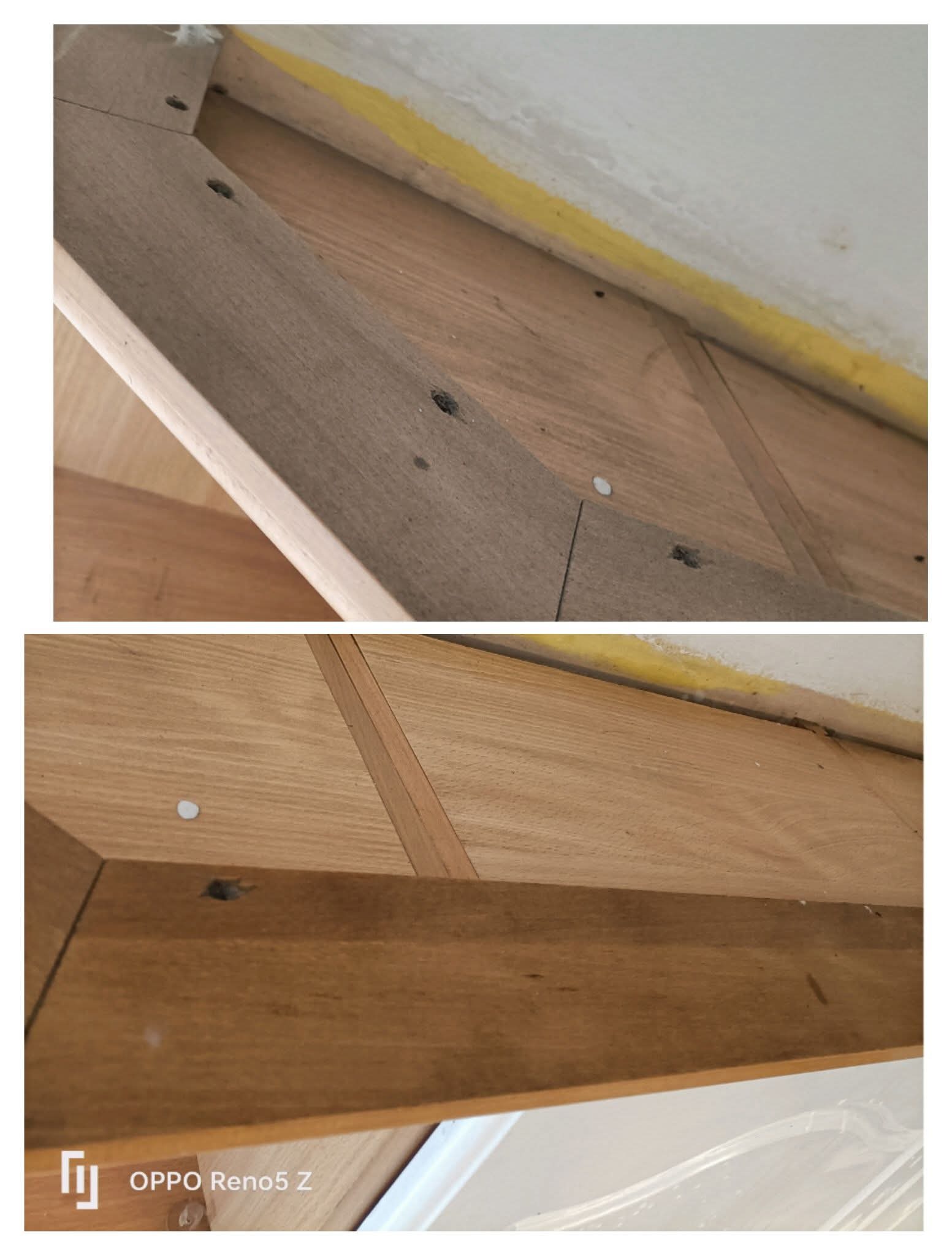 Fragment drewnianej podłogi parkietowej, z widocznymi otworami po gwoździach i śladami zabrudzeń, tuż przy ścianie z żółtą taśmą malarską.