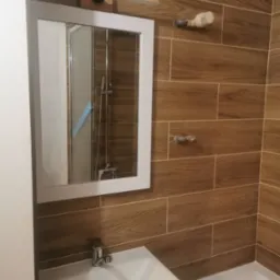 Umywalka z baterią i lustro w łazience w Kluczach, ściany wyłożone płytkami imitującymi drewno.