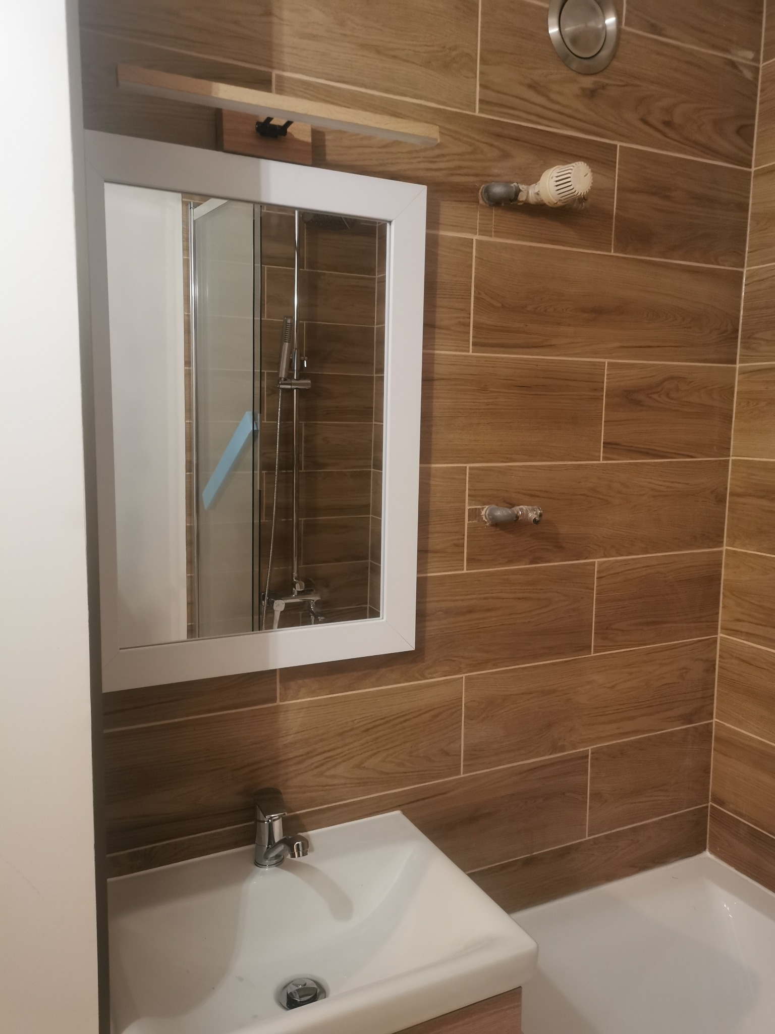 Umywalka z baterią i lustro w łazience w Kluczach, ściany wyłożone płytkami imitującymi drewno.