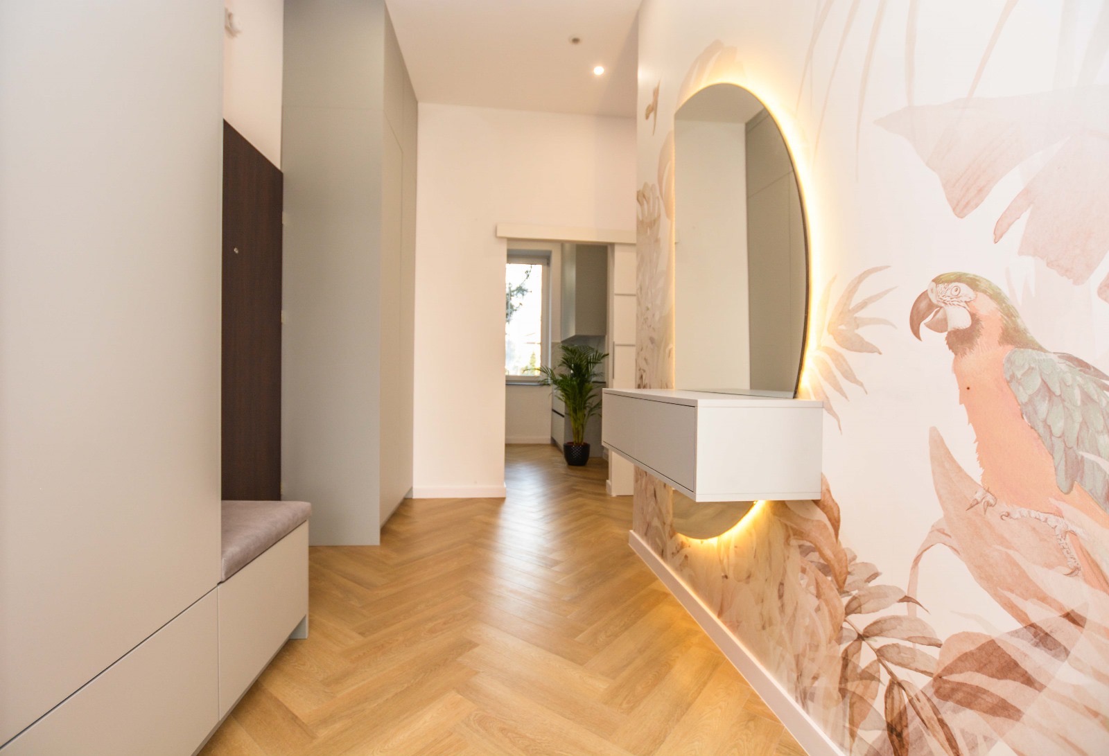 Nowoczesny przedpokój z parkietem w jodełkę, szafą wnękową, okrągłym lustrem z podświetleniem LED i tapetą z motywem papugi.