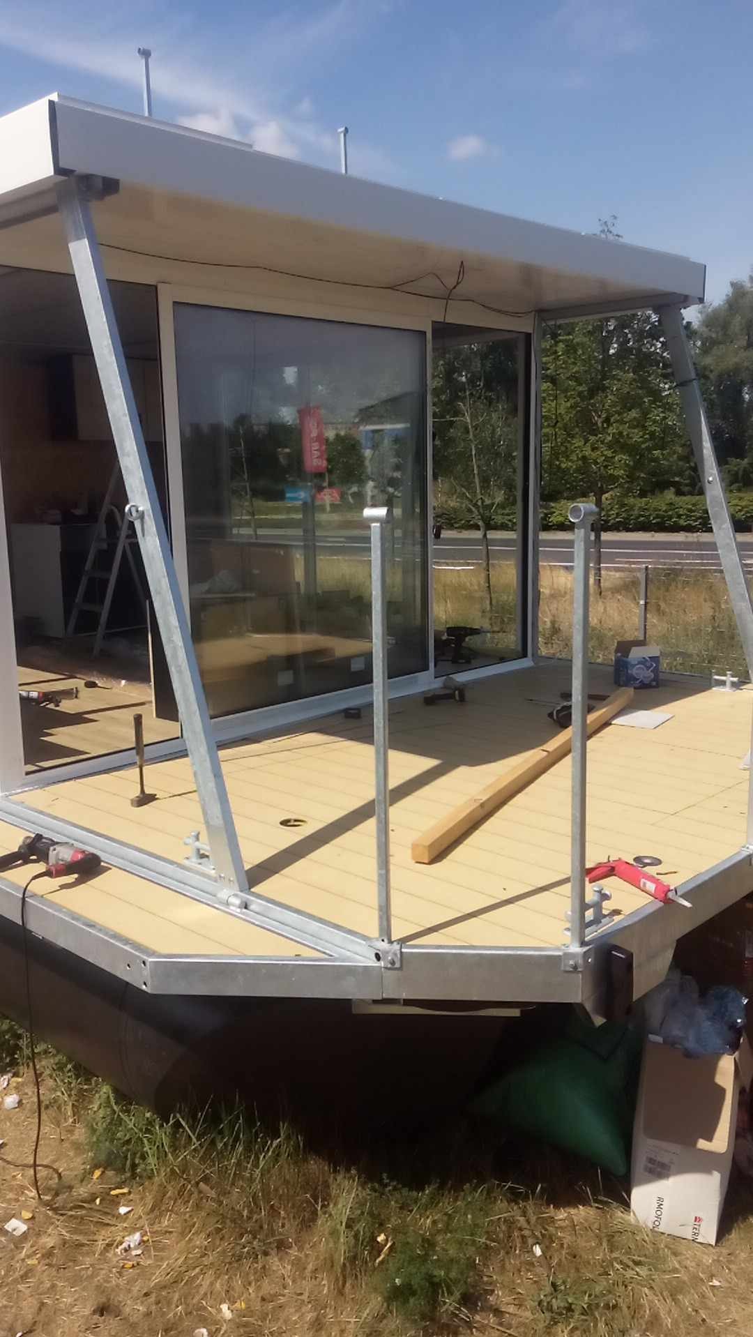 Montaż płyty warstwowej: fragment konstrukcji z metalowym szkieletem, żółtą podłogą i narzędziami. Widoczne elementy mocujące i okno przesuwne.