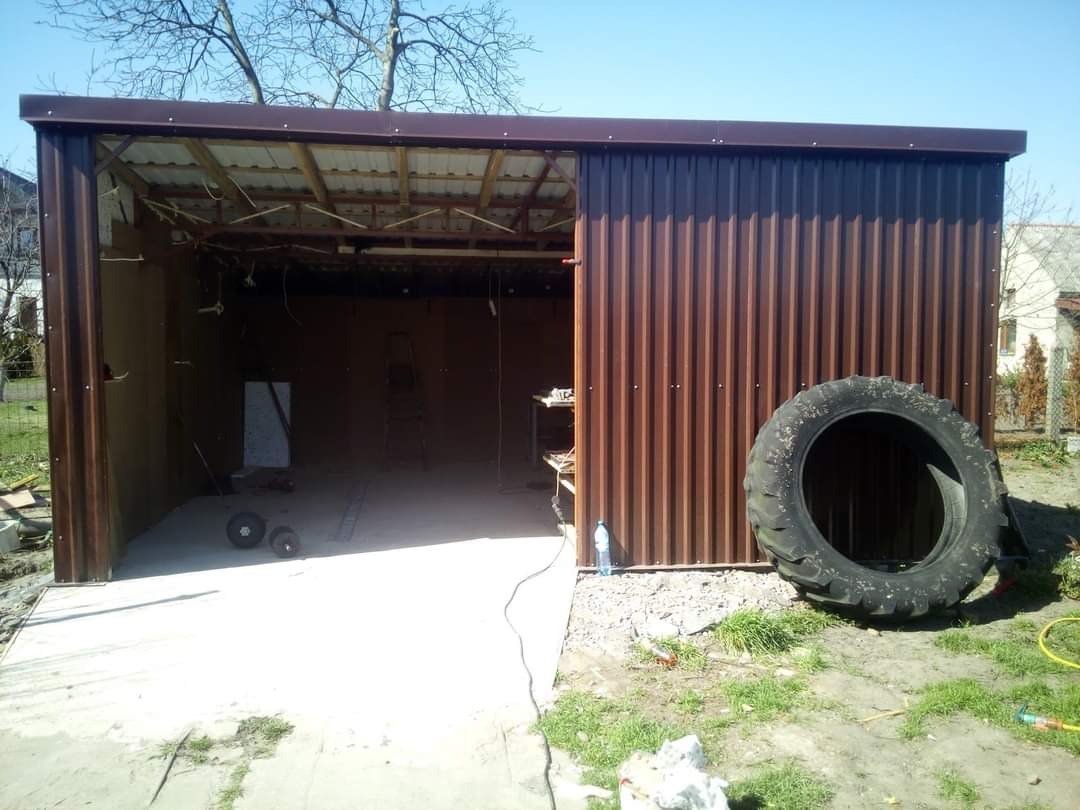 Konstrukcja z brązowych płyt warstwowych w trakcie budowy, widoczne elementy szkieletu i opona obok. Jasne niebo w tle.