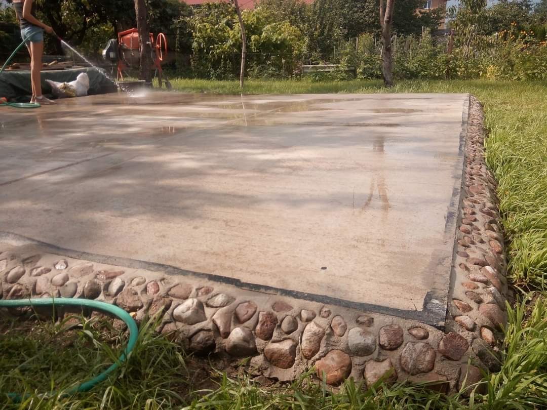 Wylewka betonowa z kamienną obwódką, czyszczona wodą pod ciśnieniem. W tle betoniarka i osoba z wężem. Świeżo wykonana, mokra powierzchnia.