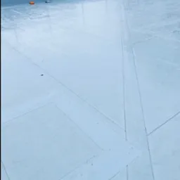 Płaski dach pokryty jednolitą, jasnoszarą membraną z widocznymi łączeniami i detalami wentylacyjnymi w tle, wykonany na budynku z ciemną elewacją.