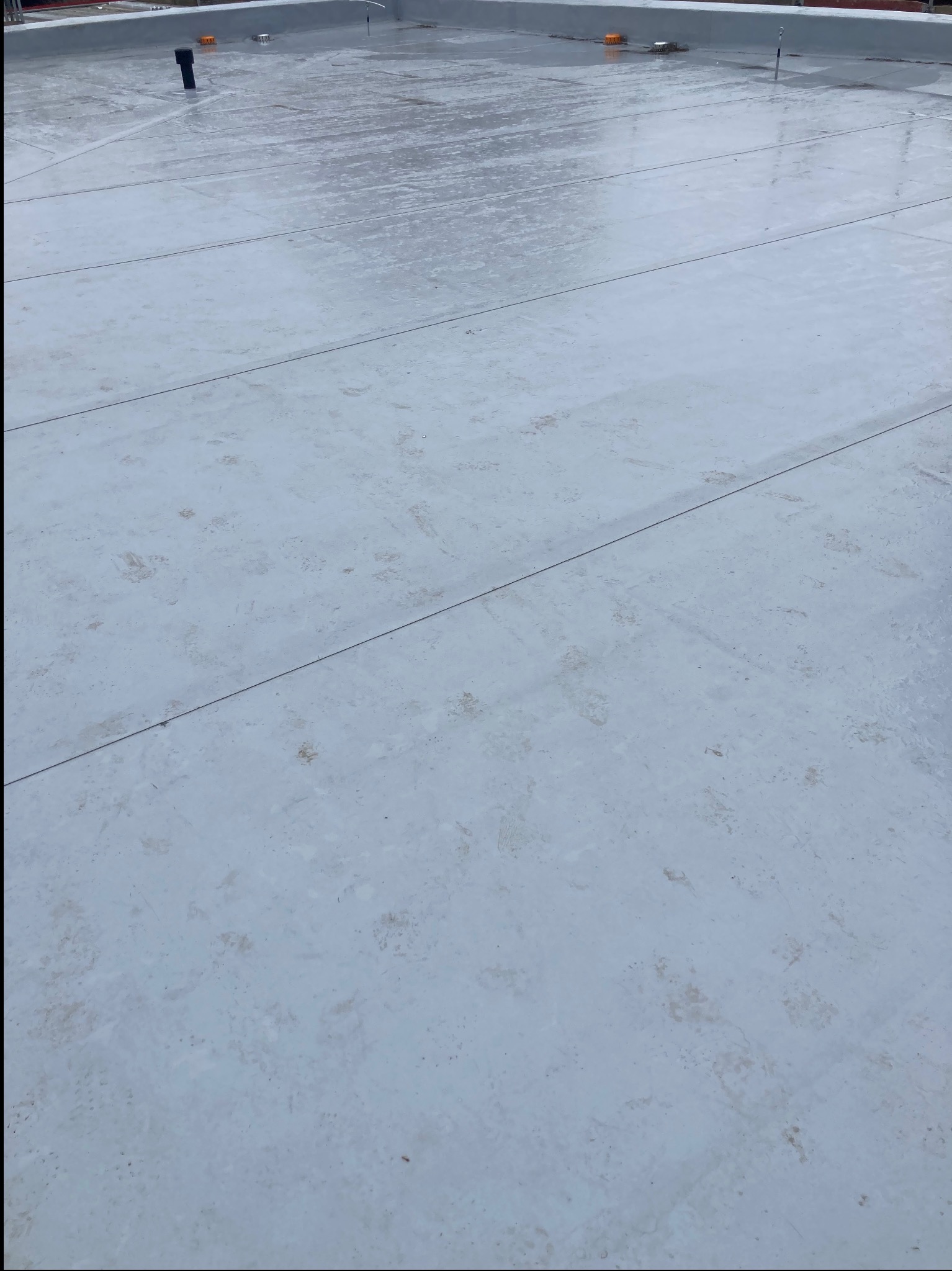 Biała, płaska powierzchnia dachu pokryta membraną, z widocznymi zgrzewami i elementami wentylacyjnymi.