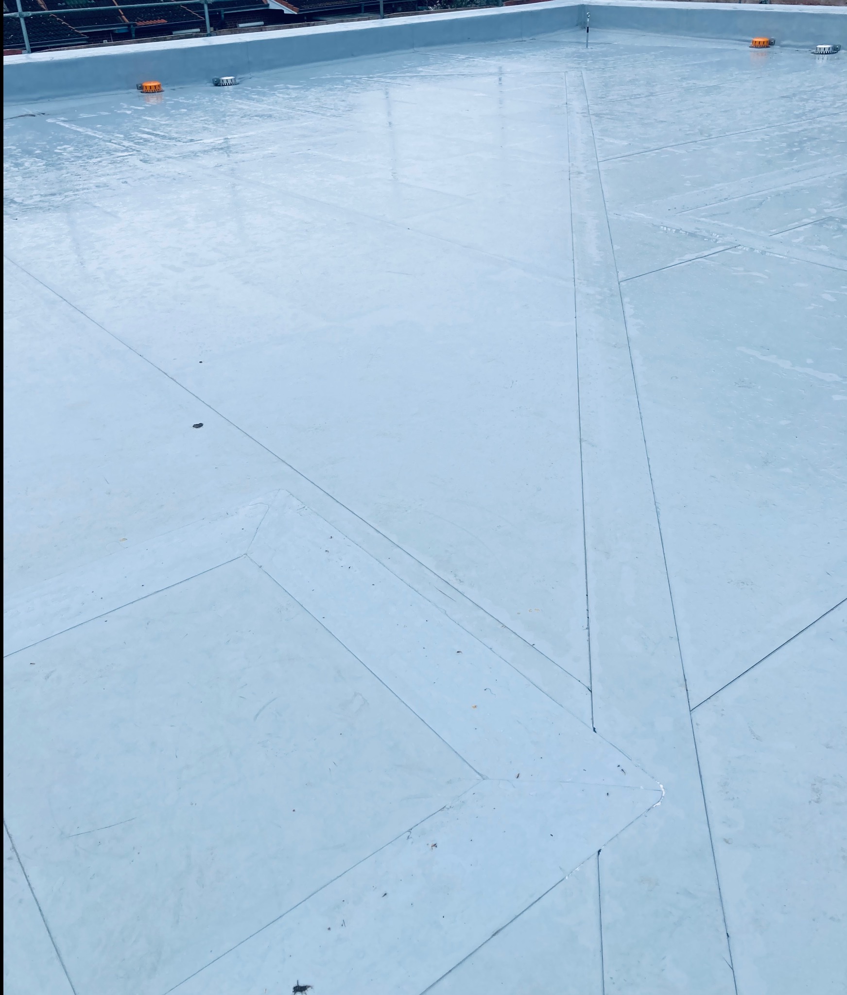 Płaski dach pokryty jednolitą, jasnoszarą membraną z widocznymi łączeniami i detalami wentylacyjnymi w tle, wykonany na budynku z ciemną elewacją.