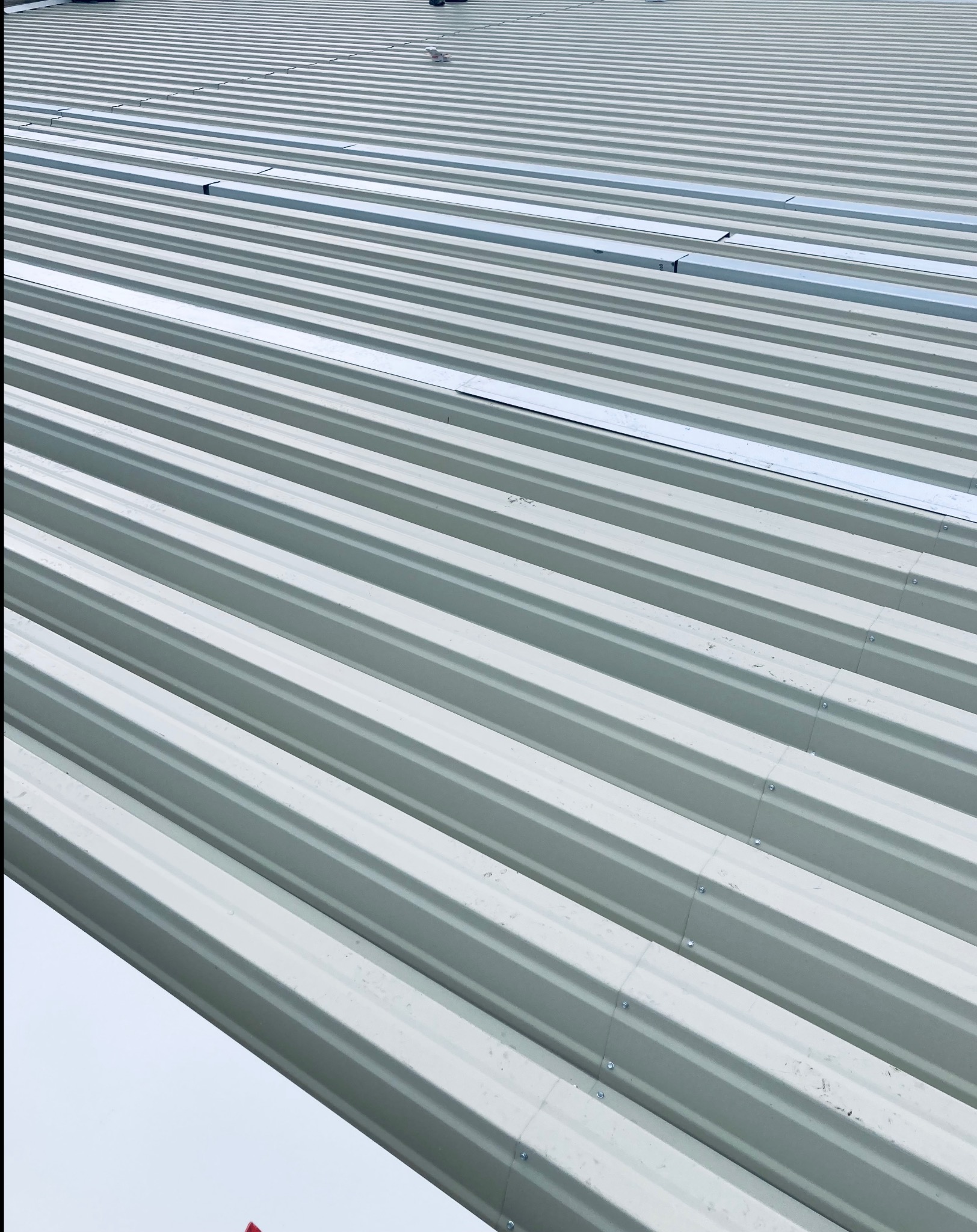 Szary dach z blachy trapezowej, widoczne łączenia i śruby mocujące, ułożony ukośnie.