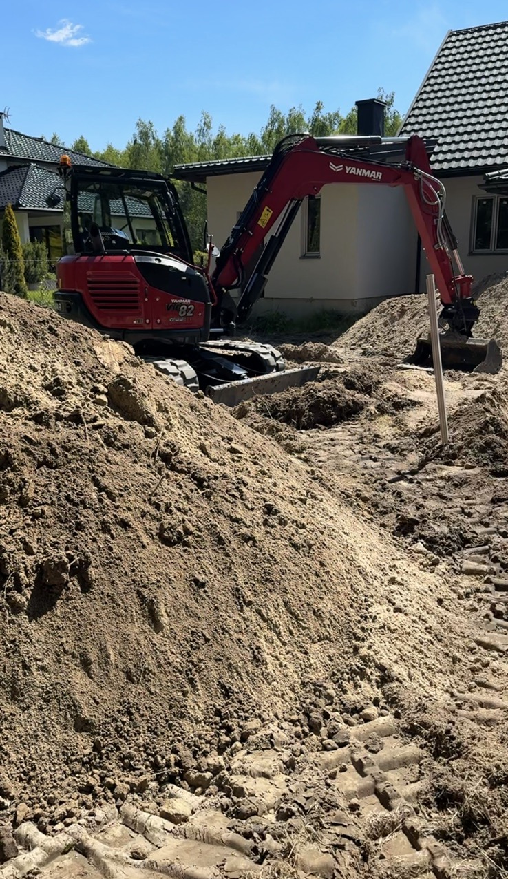 Czerwona mini koparka Yanmar na placu budowy w Wyszkowie. Wykop pod fundamenty domu jednorodzinnego, ziemia usypana w pryzmę. Słoneczny dzień.