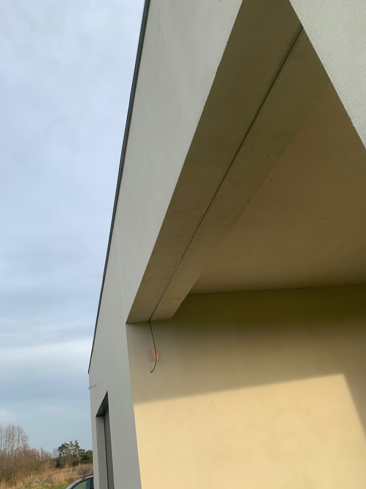 Fragment elewacji budynku z widocznym ociepleniem, świeżo po nałożeniu tynku, z wystającymi przewodami elektrycznymi przed montażem lampy.