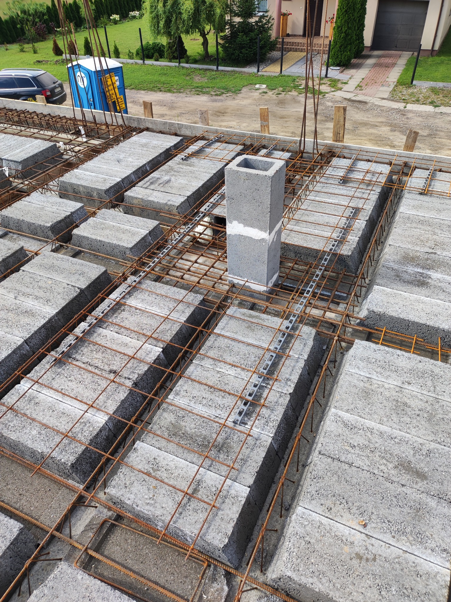 Wykonywanie stropu Teriva: betonowe pustaki ułożone w szalunku z metalowej siatki z wystającymi prętami zbrojeniowymi, widoczna także wentylacja oraz przenośna toaleta w tle.