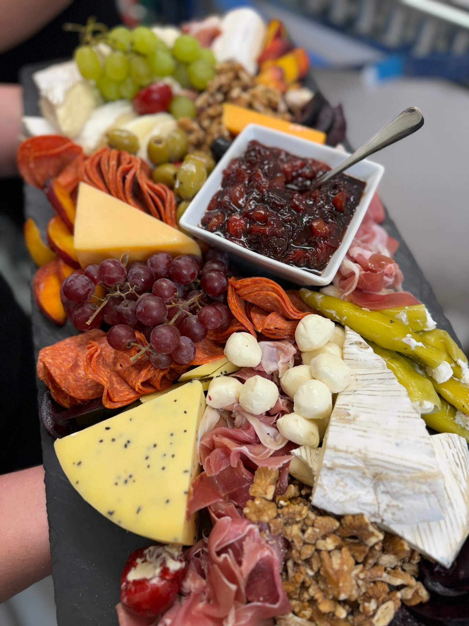 Deska serów i wędlin z owocami, orzechami i konfiturą, serwowana na czarnym łupku.