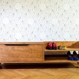 PRACOWNIA STOLARSKA MARCIN ŻEBROWSKI - Szafka na buty ze sklejki z siedziskiem, wykończona bejcą olejną i olejowoskiem. Na półkach widoczne buty. Tło stanowi ściana z geometrycznym wzorem.