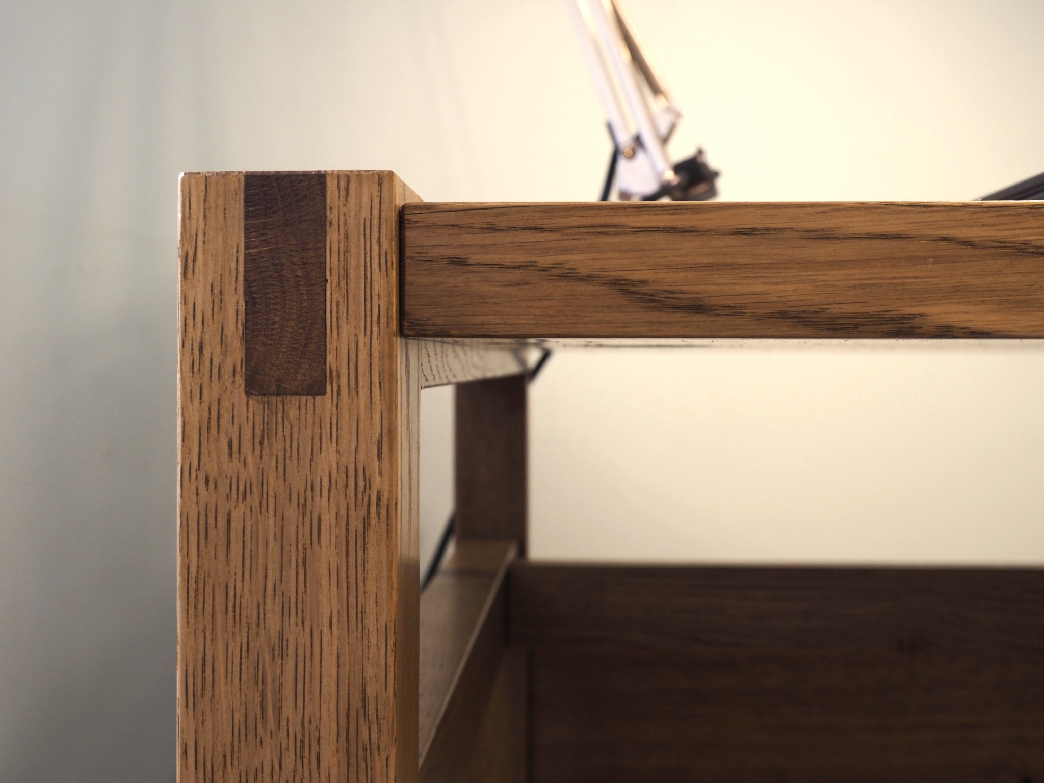 Detal dębowego biurka: solidna noga z widocznym wczepem, bejcowana i olejowana, z delikatnym oświetleniem w tle. Precyzja wykonania.