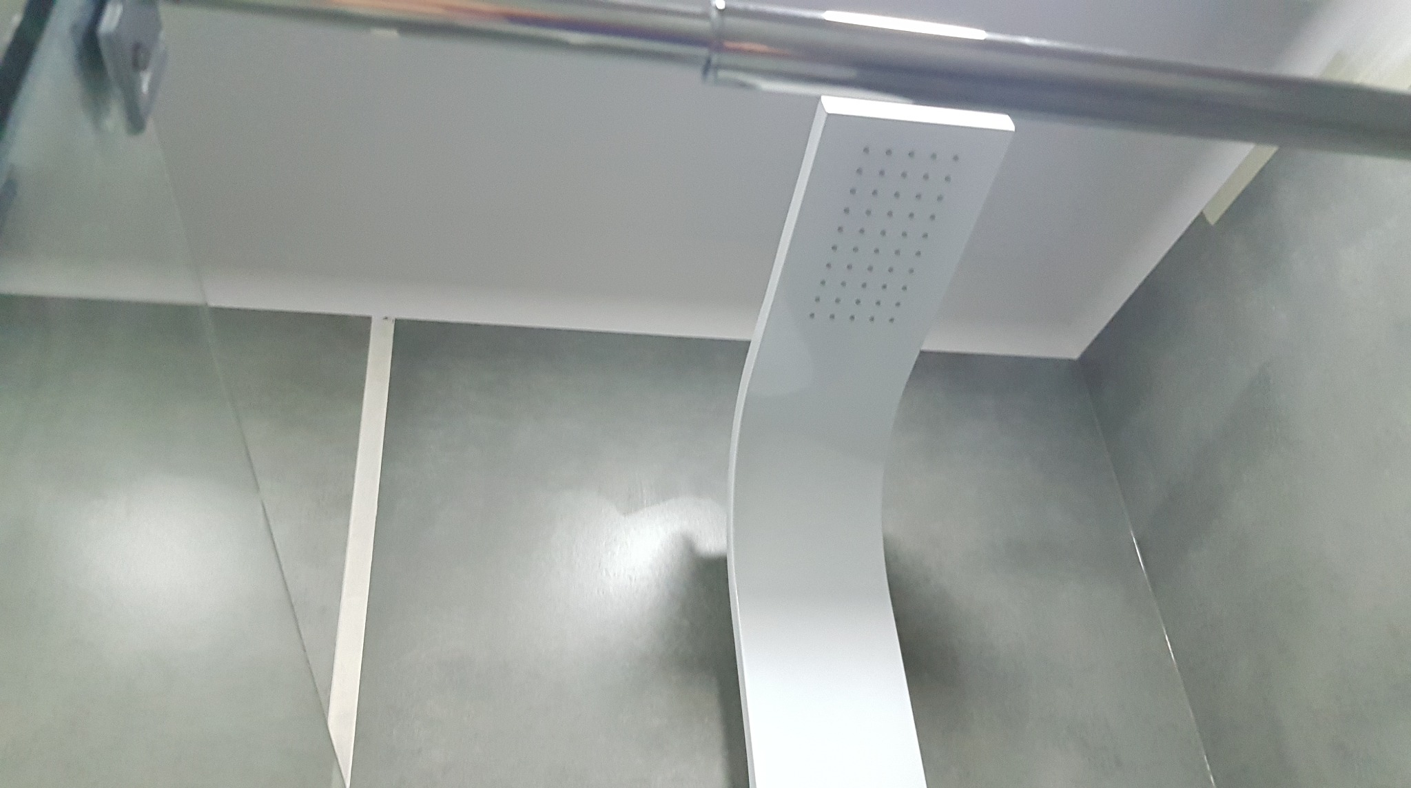 Nowoczesna deszczownica w minimalistycznej łazience z szarymi ścianami i szklanym panelem.