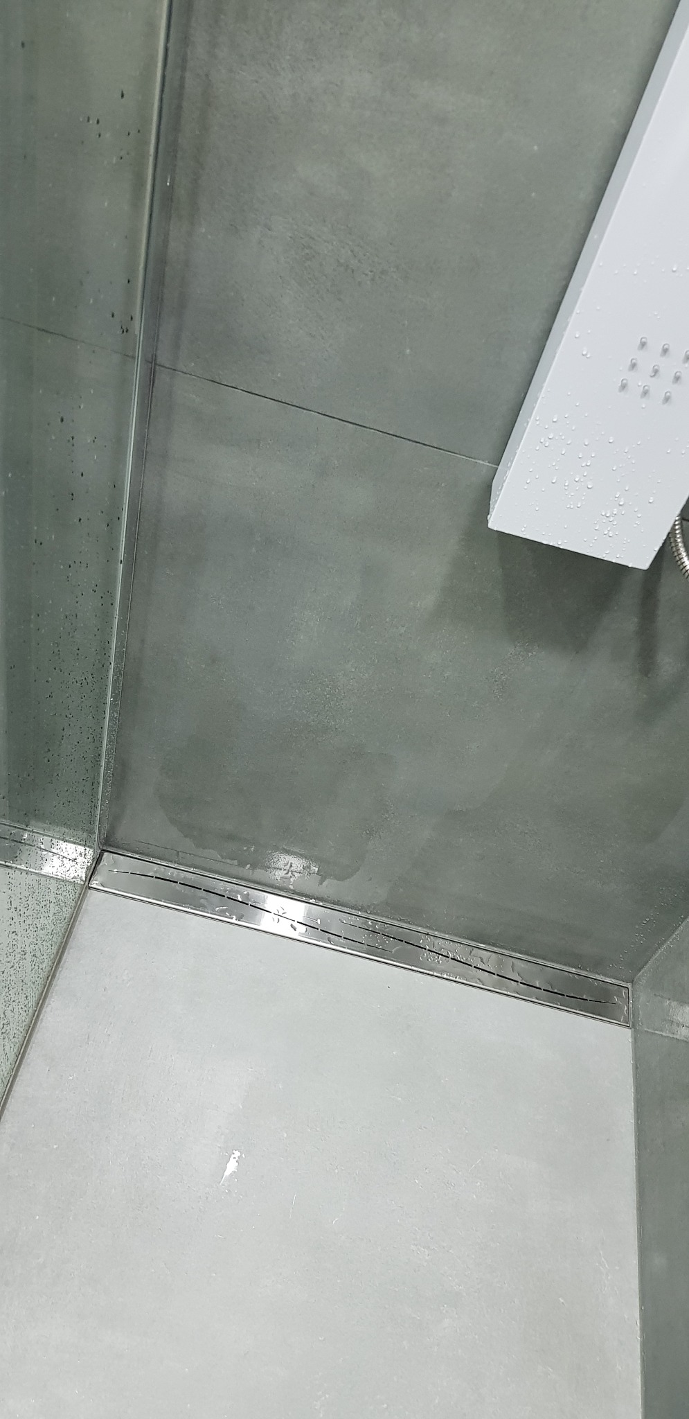Szare płytki w kabinie prysznicowej z odpływem liniowym i deszczownicą, widoczne krople wody.