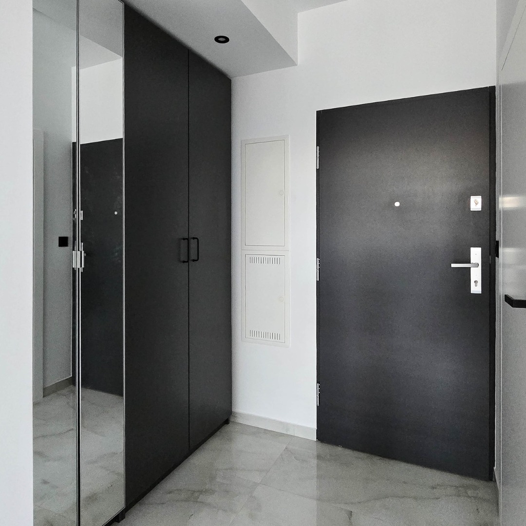 Nowoczesny przedpokój z szarą szafą, lustrem i drzwiami wejściowymi. Minimalistyczny design, marmurowa podłoga, oświetlenie punktowe. Elementy wykończenia wnętrz.