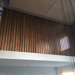 Montaż drewnianej ażurowej balustrady na antresoli z widocznym fragmentem okna i elementami konstrukcyjnymi zabezpieczonymi folią.