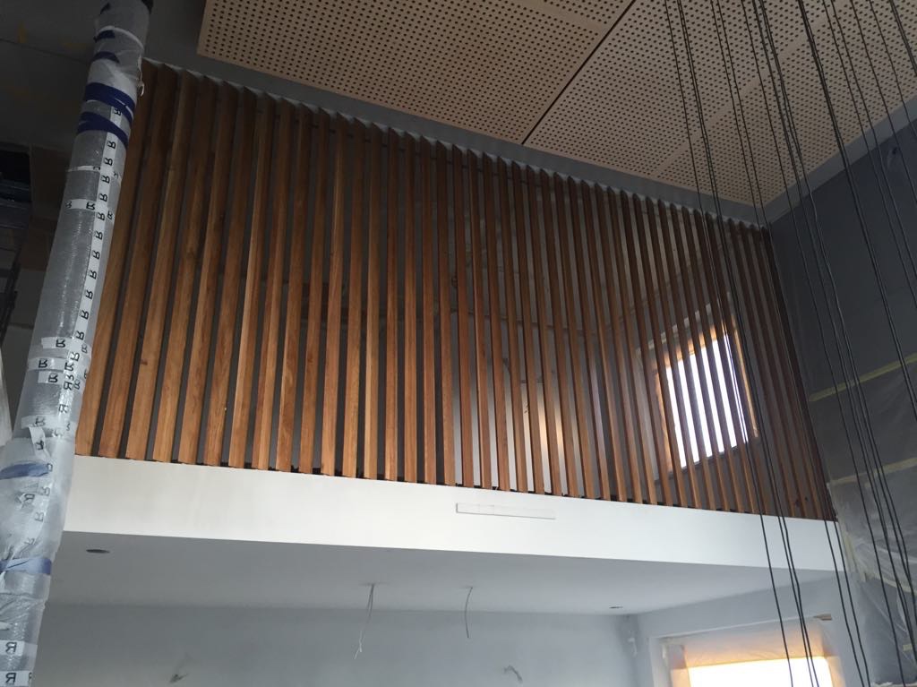 Montaż drewnianej ażurowej balustrady na antresoli z widocznym fragmentem okna i elementami konstrukcyjnymi zabezpieczonymi folią.