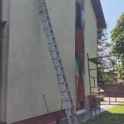PB-Cleaner - Mycie elewacji domu jednorodzinnego z użyciem myjki ciśnieniowej, widoczna drabina oparta o ścianę, okna zabezpieczone folią.