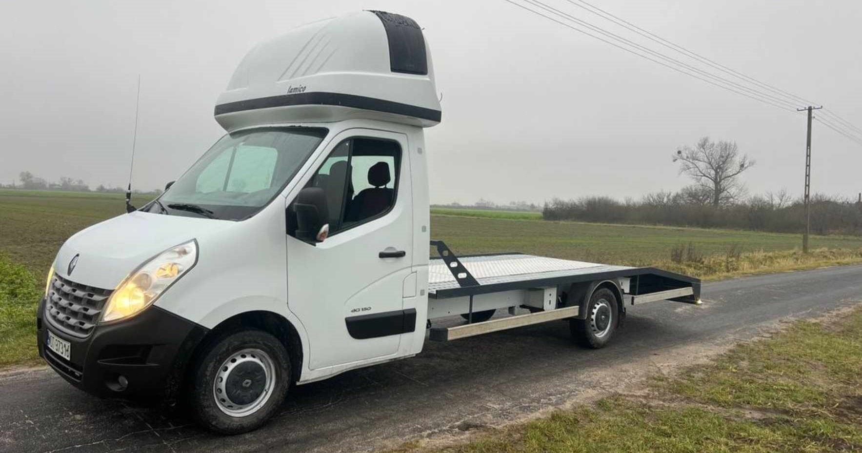 Biała laweta Renault Master z zabudową Lamice na poboczu drogi, widok z przodu, szare niebo w tle.