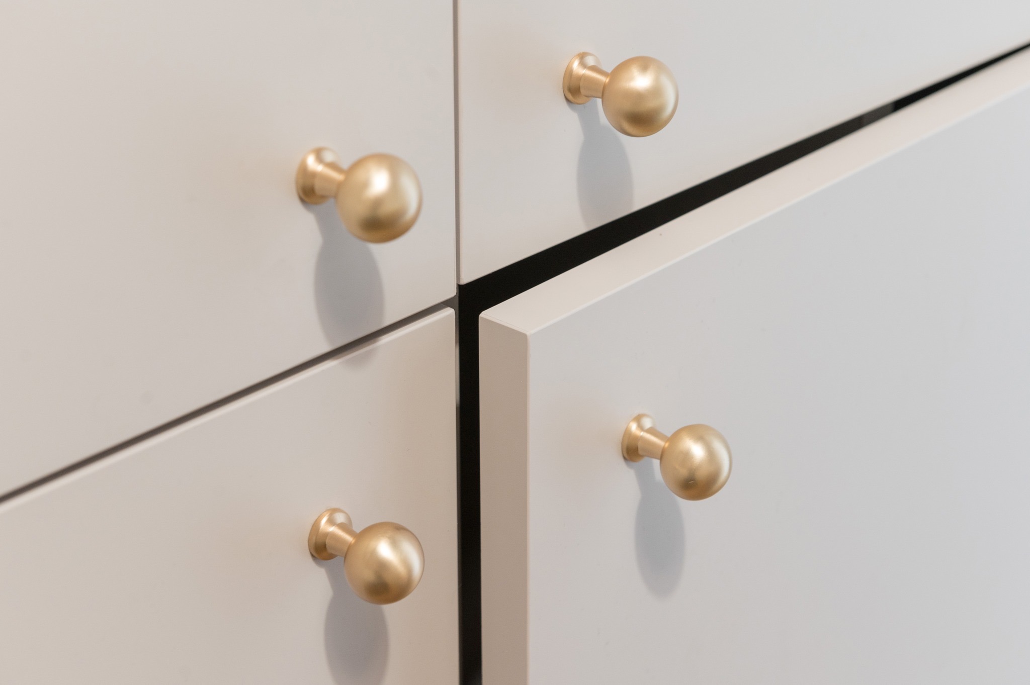 Szczegółowe ujęcie białych szuflad z okrągłymi, złotymi uchwytami, jedna szuflada lekko otwarta, ukazująca czarne wnętrze.
