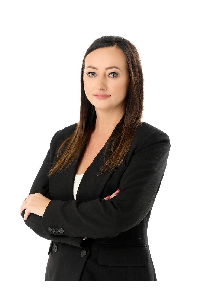 Portret kobiety w czarnym żakiecie, z założonymi rękami, na białym tle.