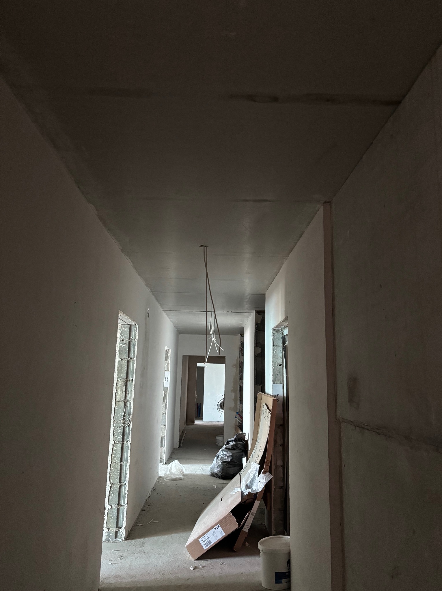 Wnętrze w trakcie remontu: surowy korytarz z widocznymi przewodami elektrycznymi zwisającymi z sufitu, przygotowany do dalszych prac wykończeniowych.