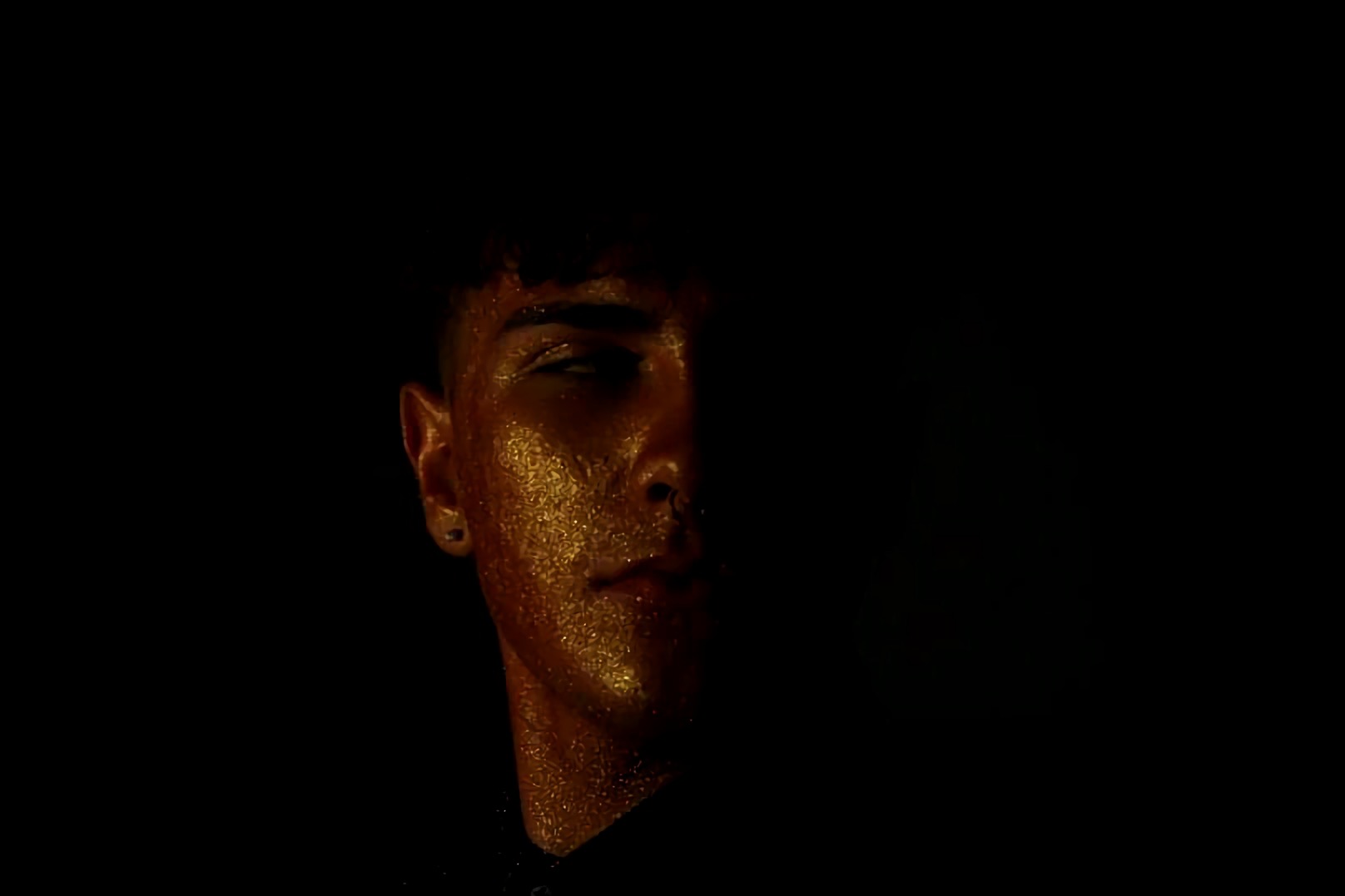 Portret mężczyzny z połową twarzy w cieniu i złotym brokatem na skórze, wykonany w Zielonej Górze.