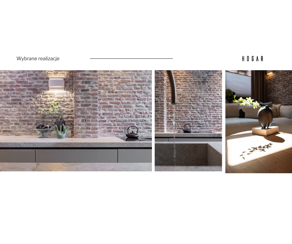 Nowoczesna kuchnia z ceglaną ścianą, szarymi szafkami i kamiennym blatem, uzupełniona dekoracjami w postaci wazonów i czajnika, z widocznym fragmentem salonu z sofą i kwiatami w tle.