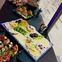 Warszawa: Dekoracyjna deska serów, warzyw i owoców na stole, obok mini burgery i przekąski, przygotowana na przyjęcie.