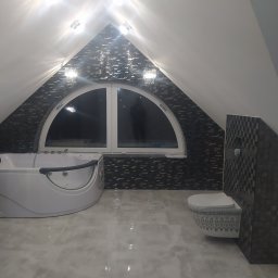 Włodar - Bud Artur Włodarczyk - Wykończona łazienka na poddaszu ze spadzistym sufitem, mozaiką na ścianach, owalnym oknem, białą wanną z hydromasażem i podwieszaną toaletą z dekoracyjnym wzorem.