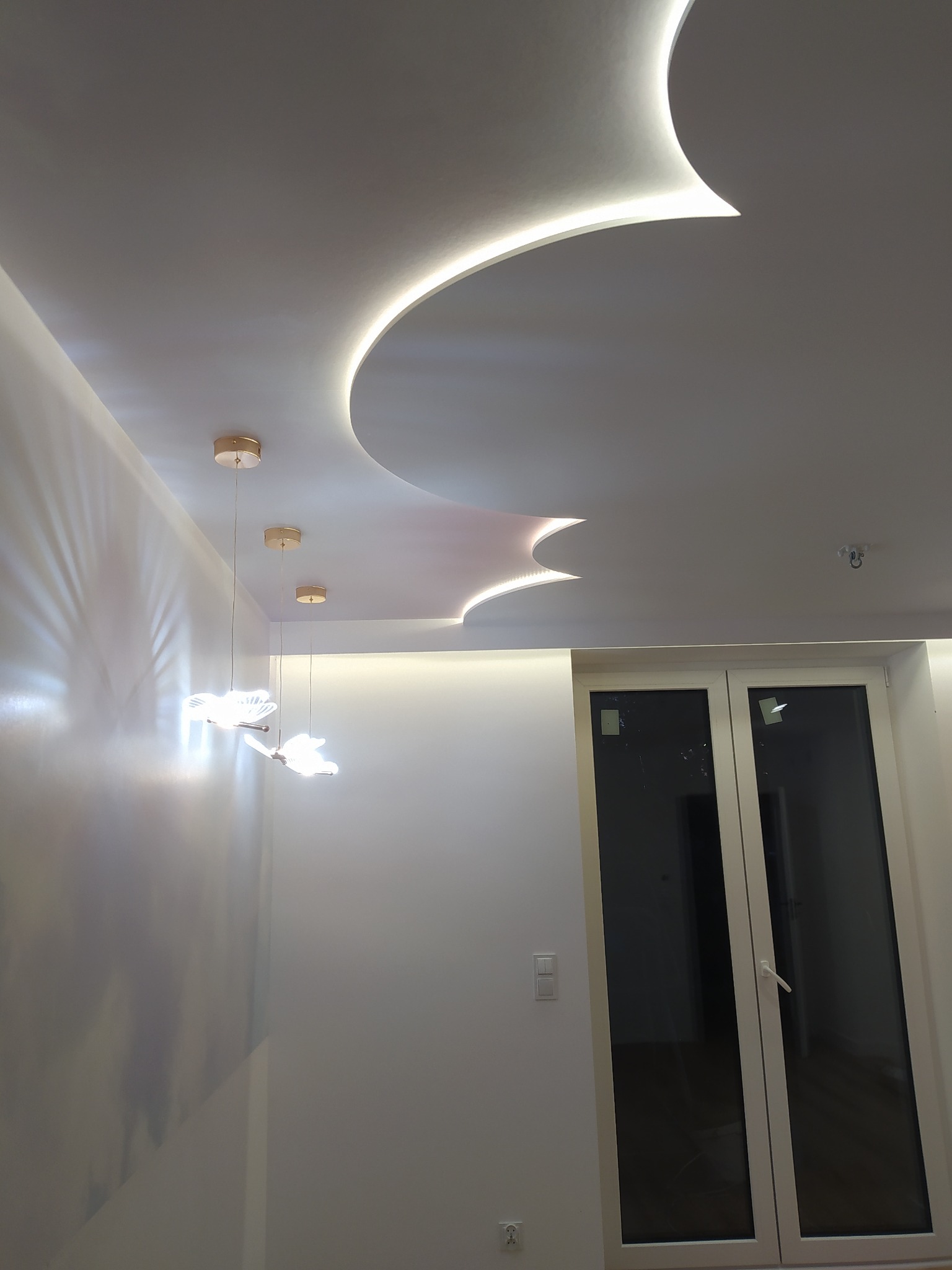 Nowoczesne wnętrze z dekoracyjnym podwieszanym sufitem z oświetleniem LED i trzema wiszącymi lampami w kształcie motyli.