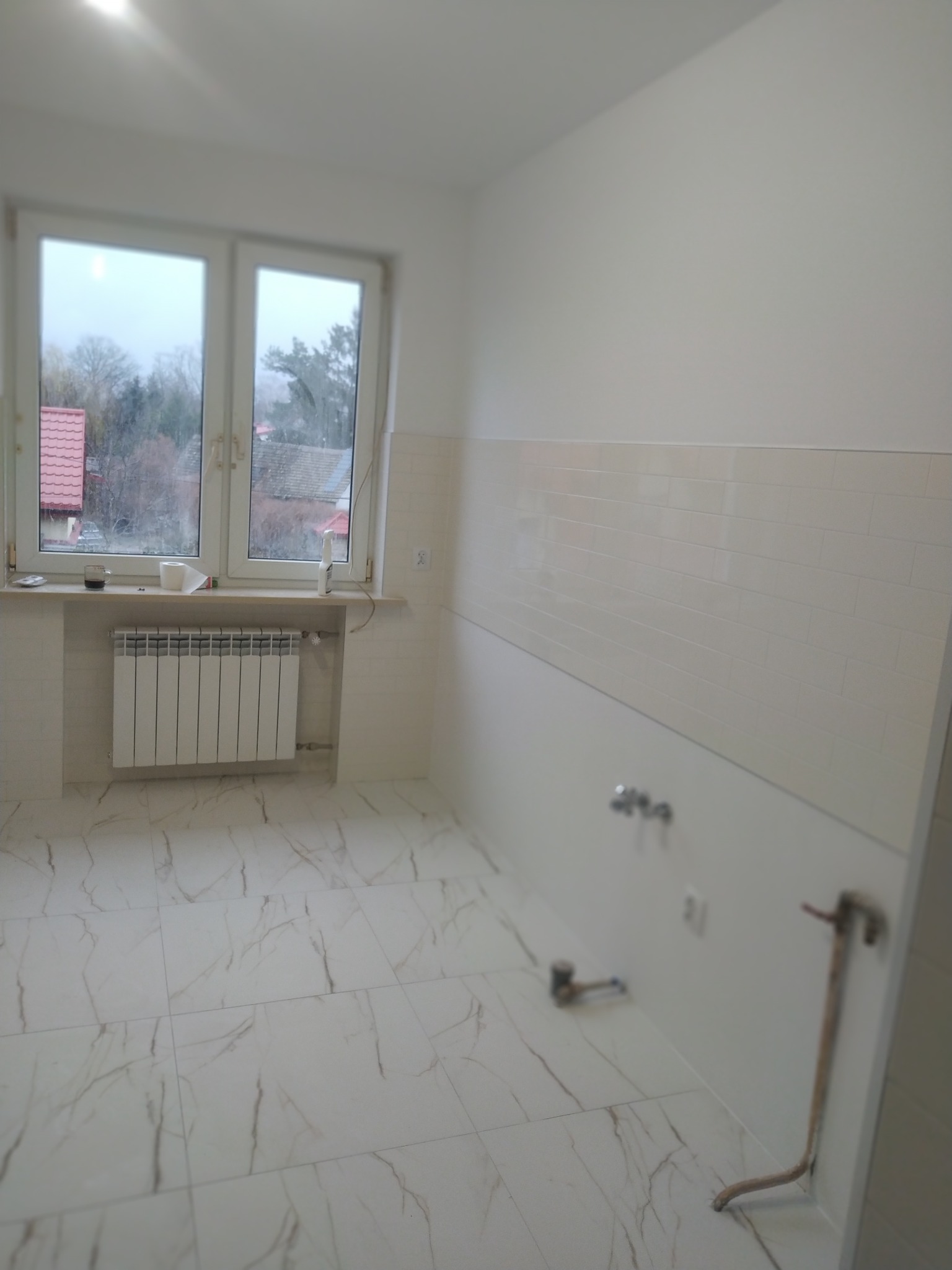 Wykończone wnętrze łazienki w Sulejówku z białymi płytkami imitującymi cegłę na ścianach, marmurową podłogą i grzejnikiem pod oknem.