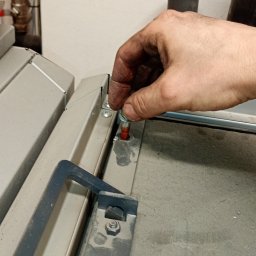 INSTAL-PARTNER Technika Grzewcza i Sanitarna Radosław Hązła - Brudna dłoń montera dokręca śrubę w metalowej konstrukcji, widoczny klucz imbusowy obok.