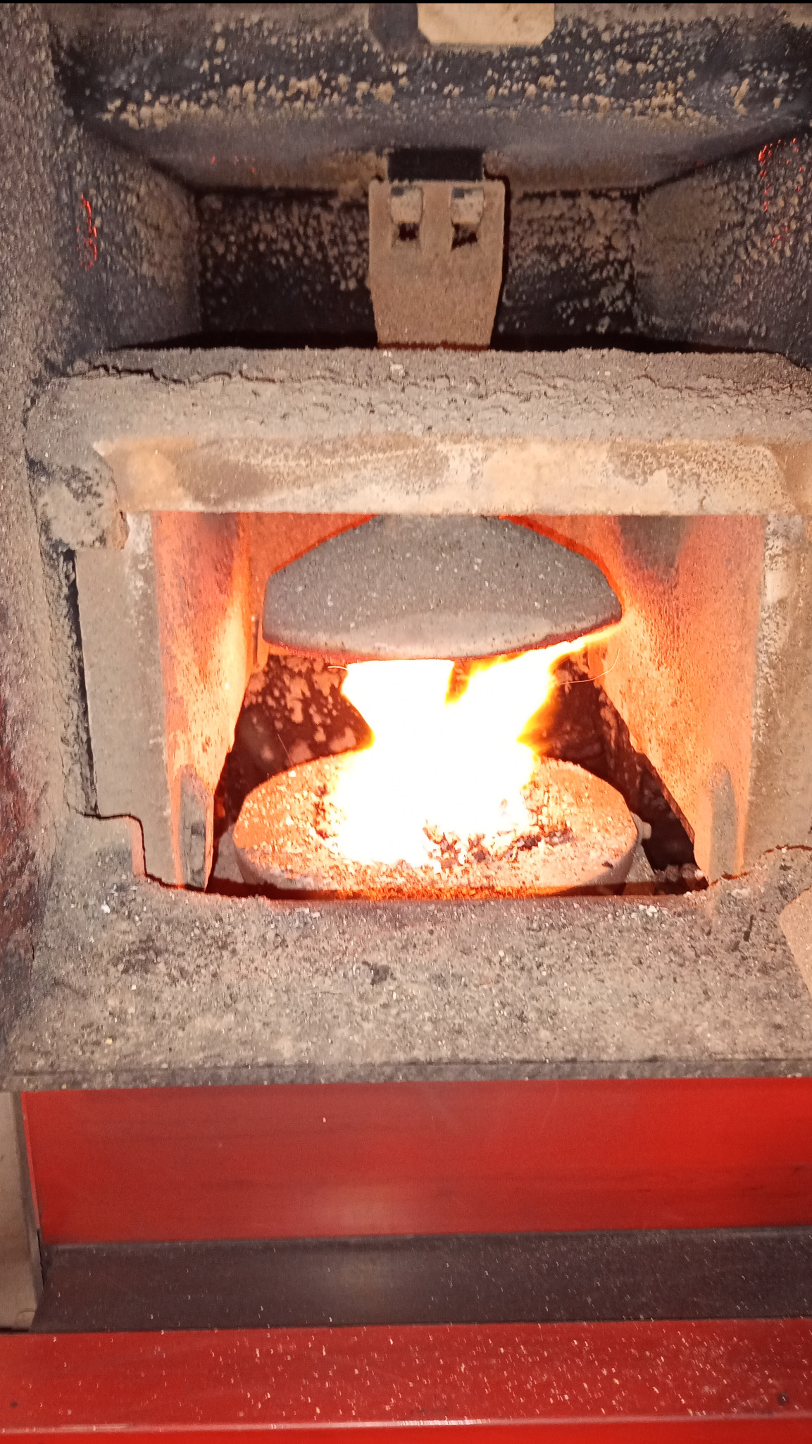 Wnętrze pieca centralnego ogrzewania z palącym się ogniem, widoczne elementy ceramiczne i żarzące się paliwo, wnętrze lekko zabrudzone popiołem.