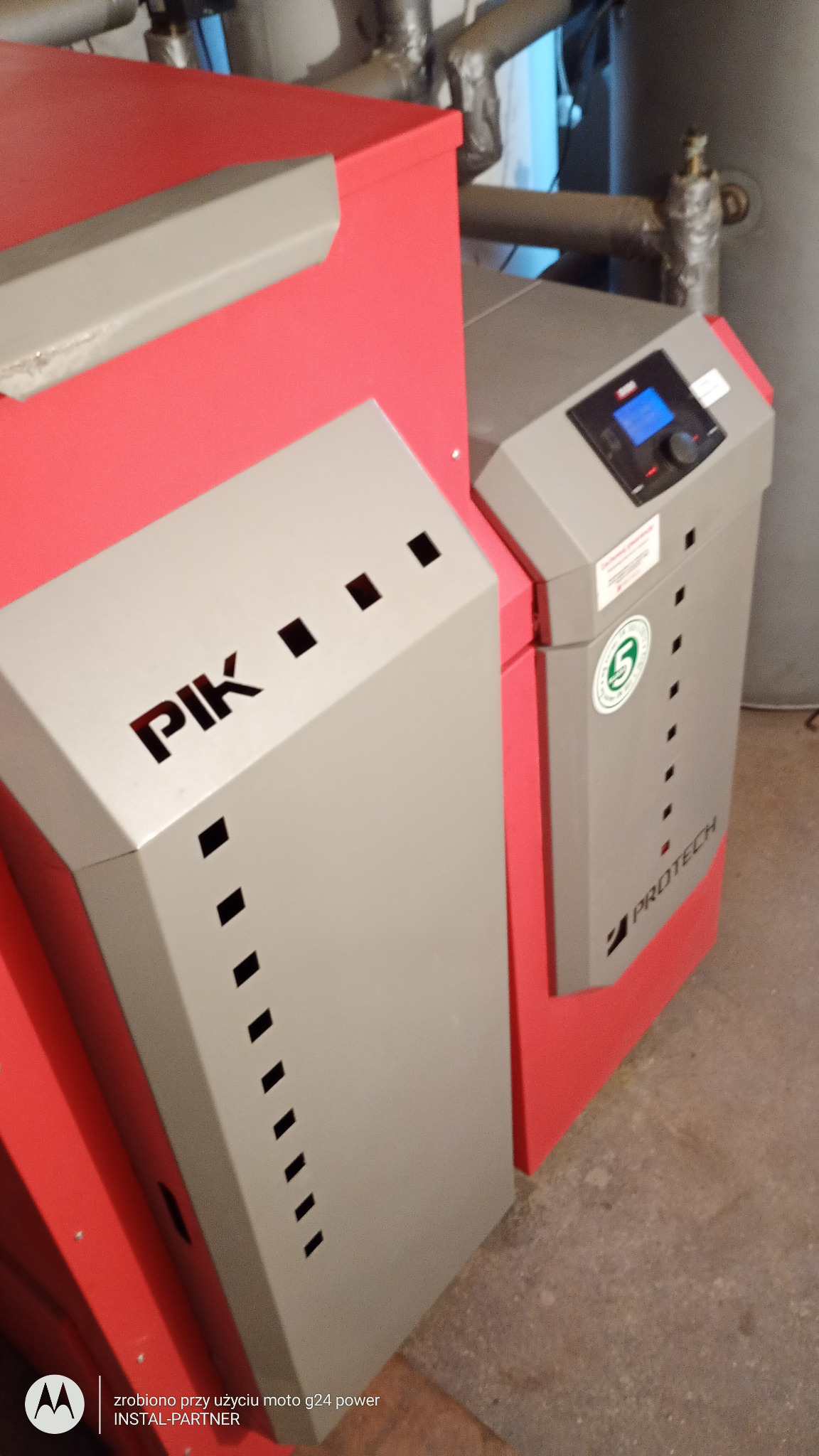 Nowoczesny piec centralnego ogrzewania marki Protech z panelem sterowania i oznaczeniem PIK, rury instalacji grzewczej w tle.