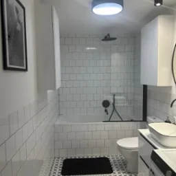 Nowoczesna łazienka z białymi płytkami typu metro, czarną armaturą, wzorzystą podłogą i minimalistycznymi szafkami.