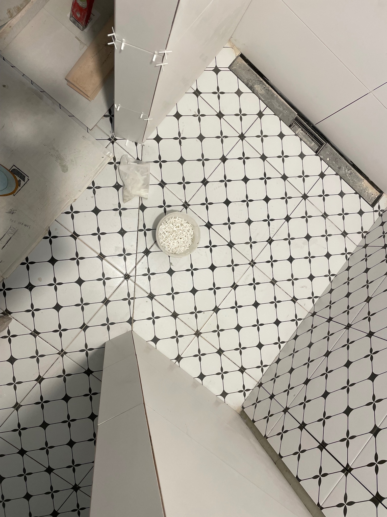 Układanie czarno-białej mozaiki podłogowej w łazience, widok z góry, widoczne krzyżyki dystansowe, odpływ liniowy i fragment zabudowy.